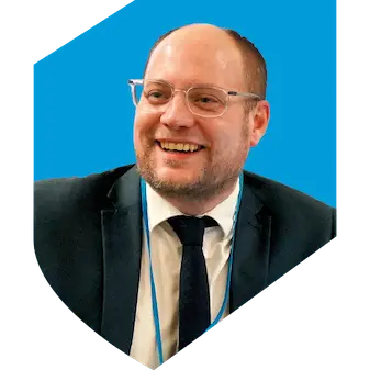 Man wearing a suit and glasses with a light blue shield in the background