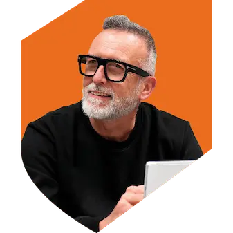 A man wearing glasses with a black top, short hair and beard sitting with an orange background in the shape of a shield.